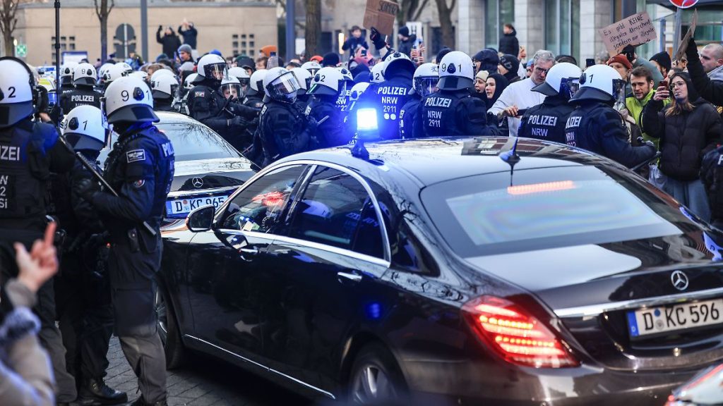 Hitze Situation in Köln: Merz Visits Clinic – Demonstranten Blockausgang blockieren